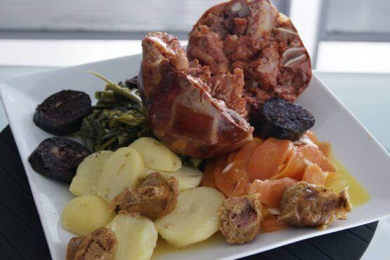 Prato com costela assada, batata fatiada, cenoura, beterraba e tufos de espinafres num prato branco.