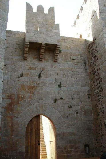 Torre de pedra medieval com porta de arco ogival e ameias no topo, integrada em muralha fortificada.