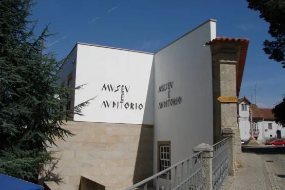 Fachada branca do Museu e Auditório com letras em parede, árvores e torre medieval ao fundo