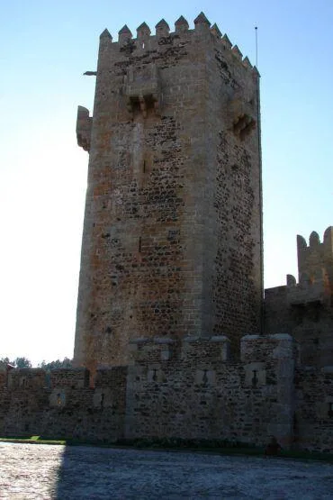 Torre de pedra quadrangular com ameias, integrada em muralha portuária junto a curso de água, sob céu limpo.