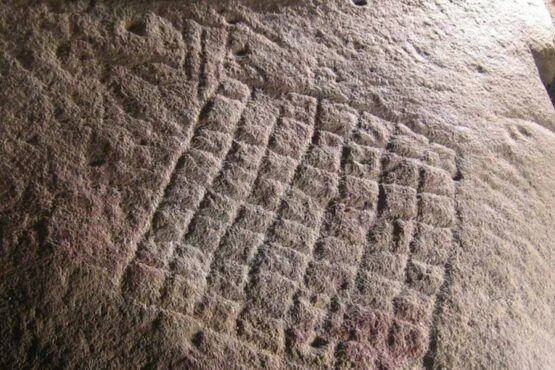 Inscrição gravada em relevo numa superfície de pedra clara, com caracteres em disposição angular.