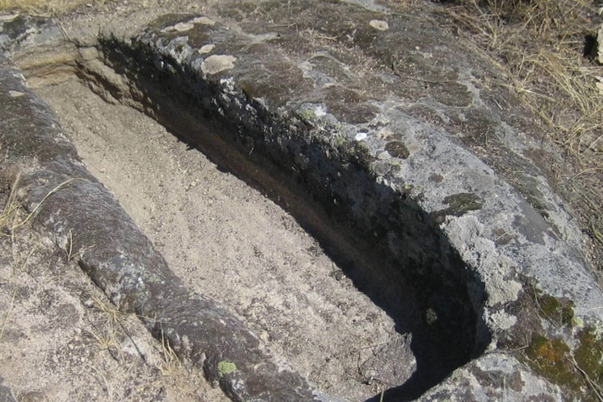 Fenda profunda em rocha calcária cinzenta com musgo e vegetação esparsa no topo
