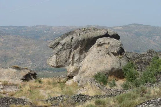 Formação rochosa granítica com aparência zoomórfica numa paisagem montanhosa beirã, com várias elevações ao fundo.