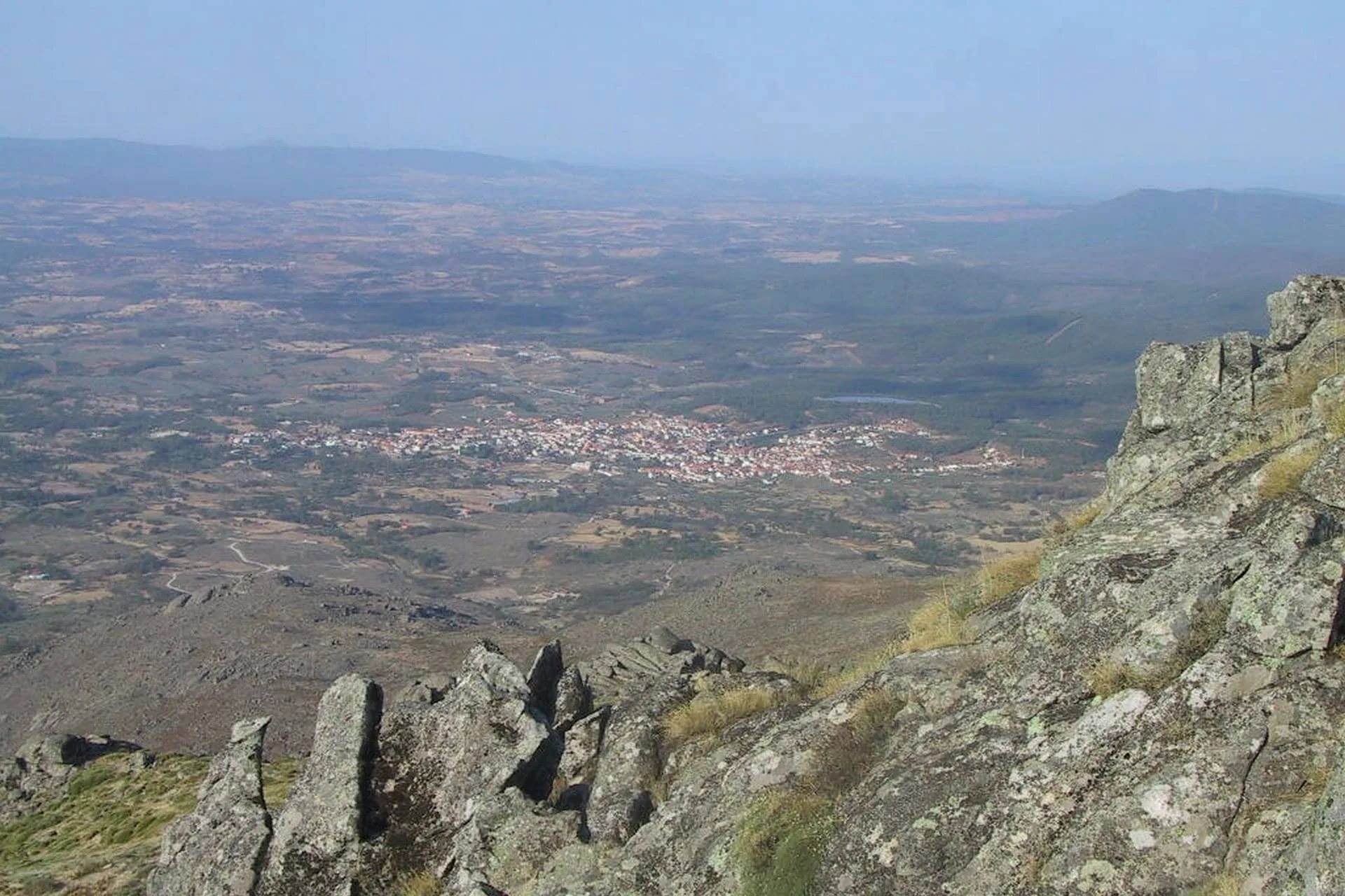 Vista aérea de uma planície agrícola desde rochedos de pedra, com uma localidade ao fundo e montes ao horizonte.