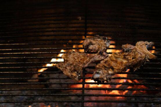 Peças de carne assada na grelha com chamas alaranjadas visíveis por baixo da grelha metálica
