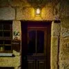 Porta de madeira escura com dois painéis e vidro, em fachada de pedra iluminada a amarelo durante a noite